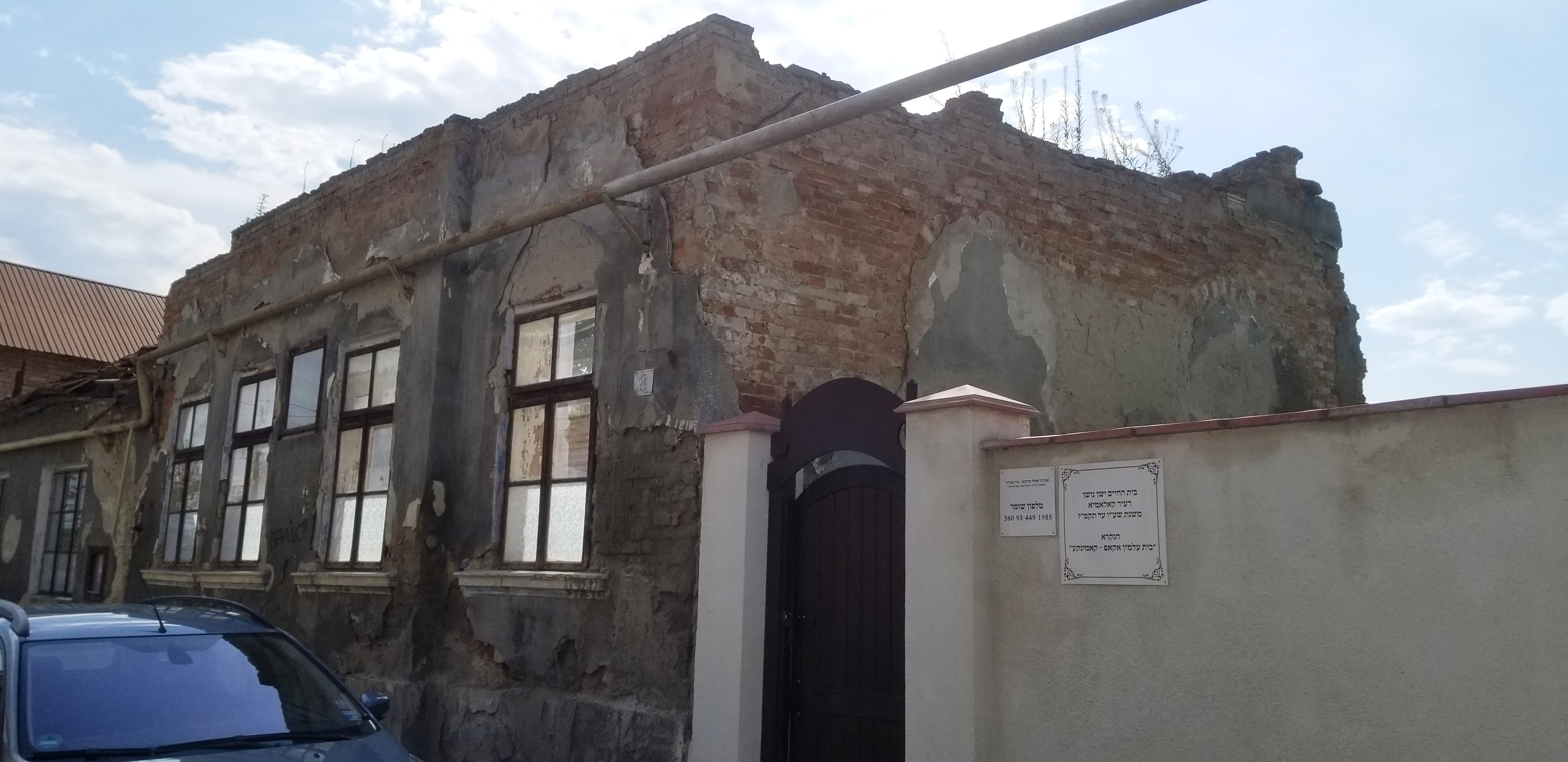 Exterior of Beit Midrash and wooden gate to
                    cemetery